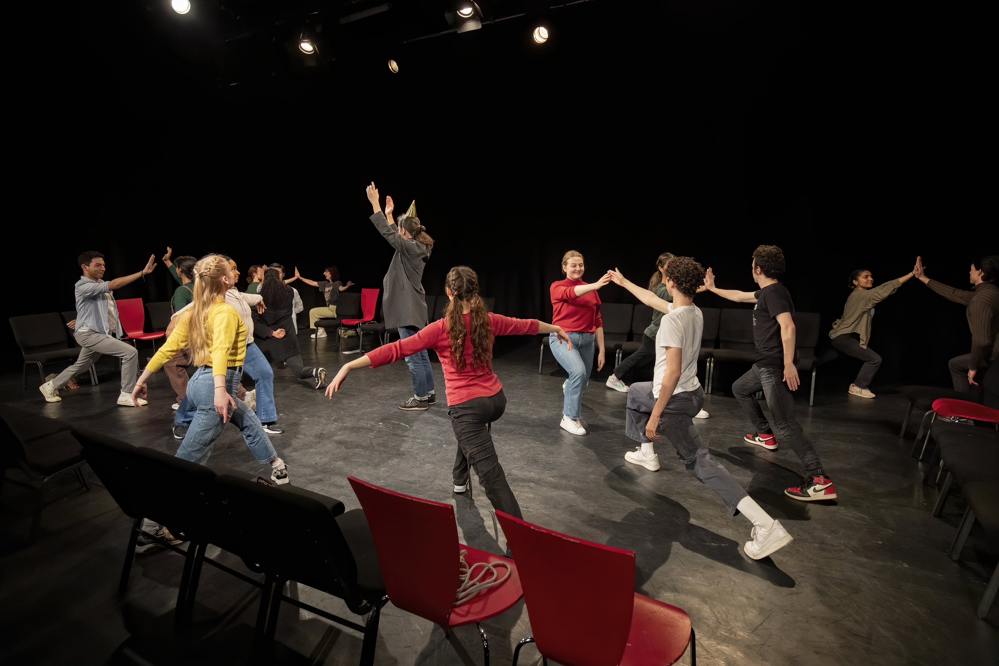 Students in mid-performance and arms outstretched in a black box theatre